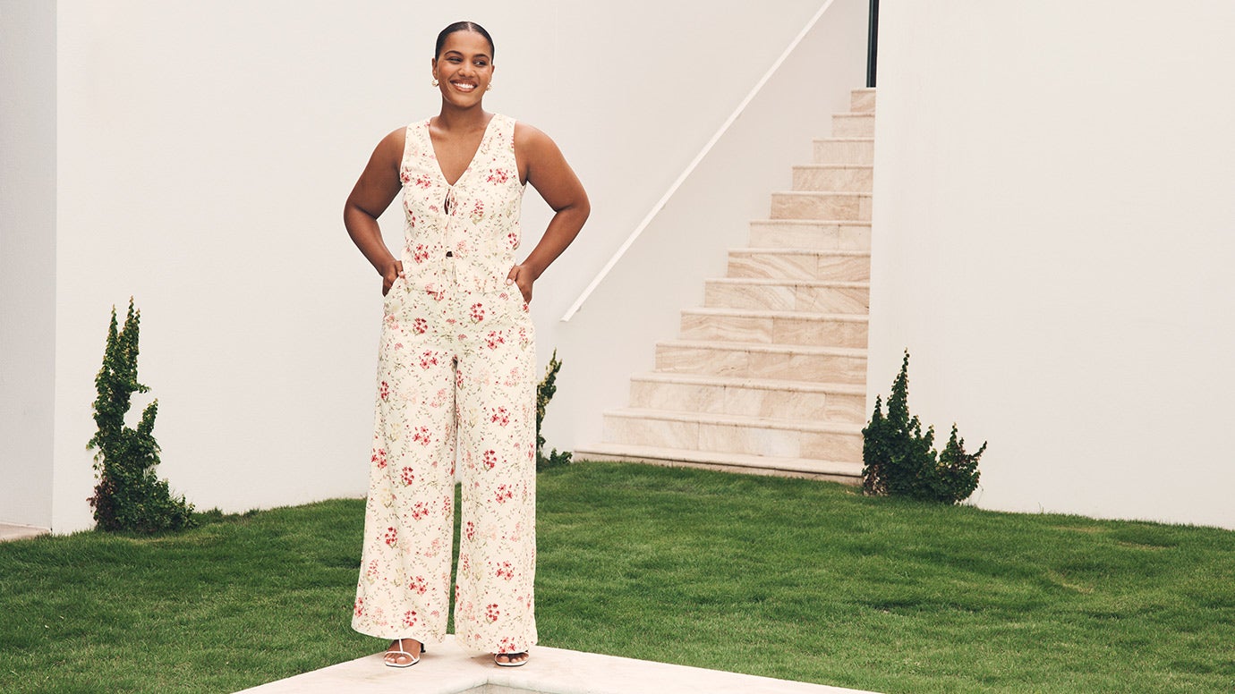 influencer and model sierra johnson wearing a relaxed resort set with wide legs pants and a tie-front vest in a delicate floral print, she is posing with hands on hips in front of some stairs and lush manicured lawn